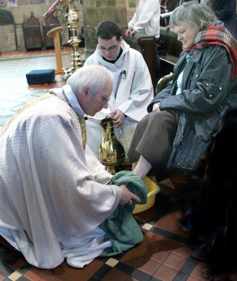 Walesi anglikán püspök egy idősebb hölgy lábát mossa